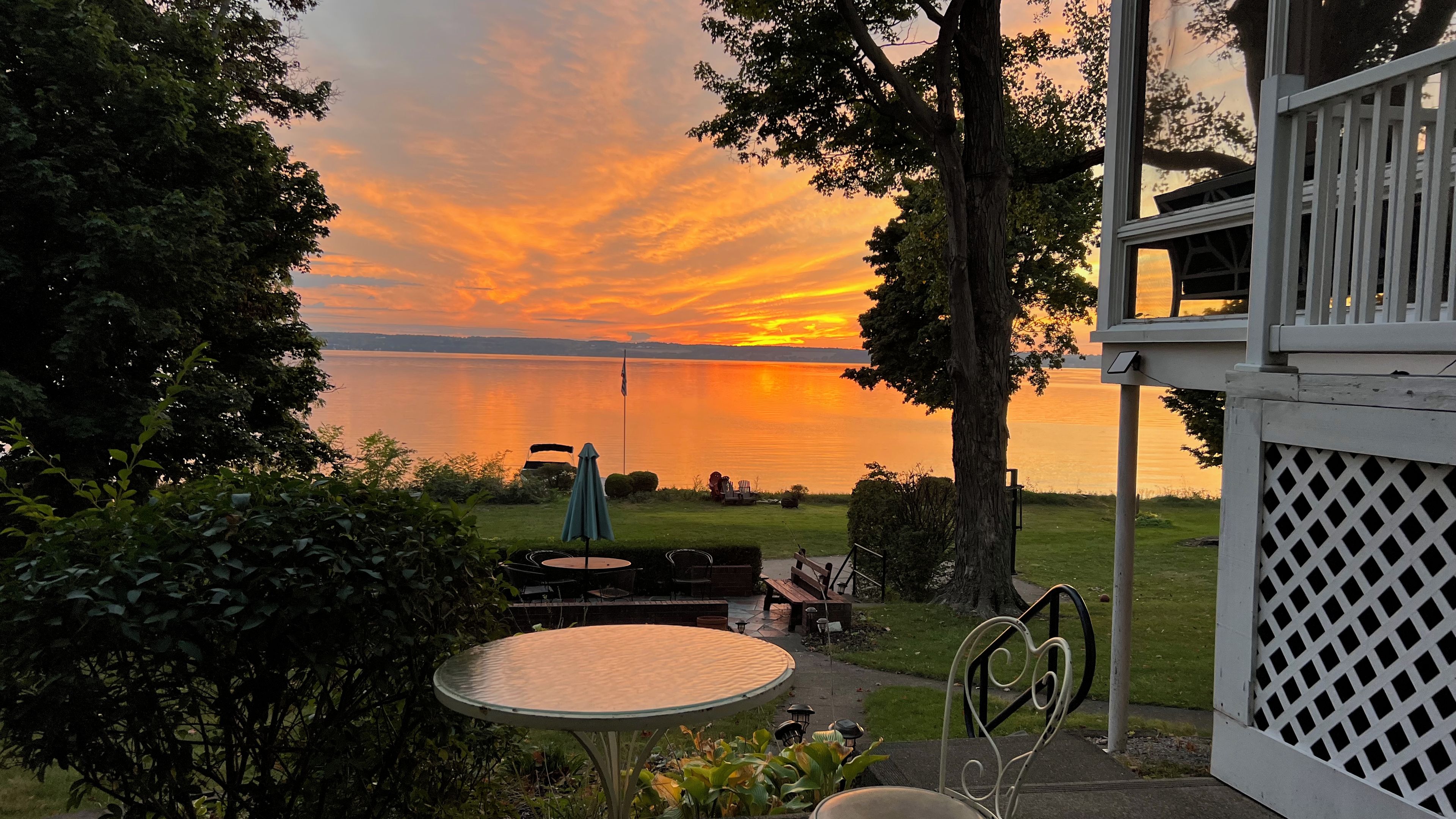 Une terrasse avec une table et des chaises, donnant sur un lac où l’on peut admirer le coucher du soleil.