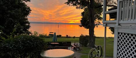 Een terras met een tafel en stoelen, met uitzicht op een meer bij zonsondergang.