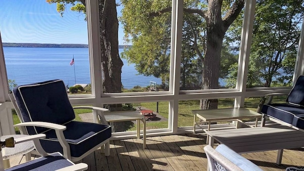 A covered deck with outdoor furniture, a view of a lake, and a flag. - Lakefront Home in the Heart of Aurora, Sunset Ready! (Aurora)