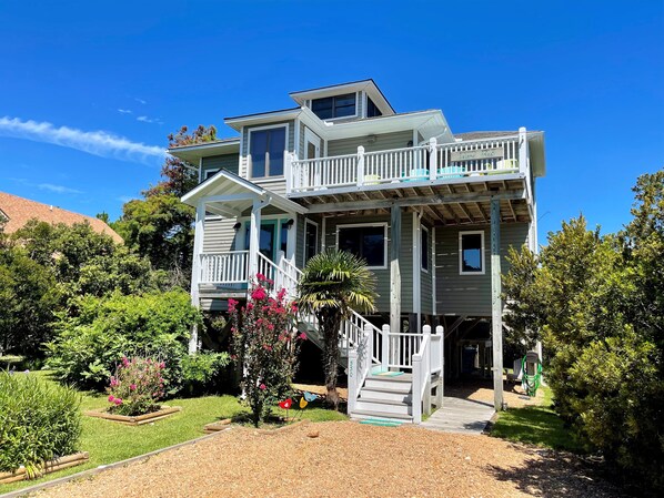 Ein zweistöckiges Haus mit Balkon, überdachter Veranda und einem Garten mit verschiedenen Pflanzen und Blumen.