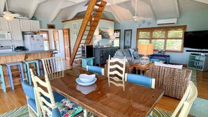 A spacious living area with a wooden dining table, blue cushioned chairs, a sofa, and a television. - Island Rest:  Marsh and distant sound views on Jackson Circle (Ocracoke)