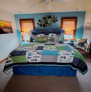 A bedroom with a blue and white quilted bedspread, a 'RELAX' sign on the bed, and a ceiling fan.