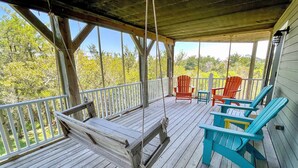A wooden deck with a swing, two red Adirondack chairs, and two blue Adirondack chairs. - Island Rest:  Marsh and distant sound views on Jackson Circle (Ocracoke)