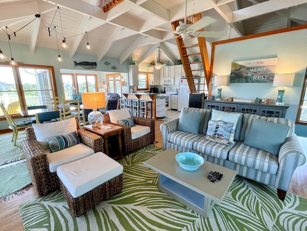 A spacious living area with a high ceiling, a kitchen in the background, and a cozy seating arrangement.