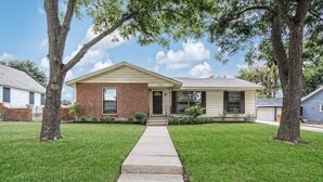 A single-story house with a front yard, a driveway, and two trees. - A perfect home for your vacation! (Waco)