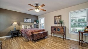 A bedroom with a wooden floor, a bed with a patterned bedspread, a nightstand with a lamp, a dresser, and a ceiling fan. - A perfect home for your vacation! (Waco)