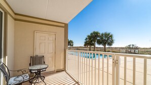 A balcony with a pool view, a door, and a table with chairs. - The Inn at Dauphin Island 106 1BR Walks right out to Pools and Beach! (Dauphin Island)