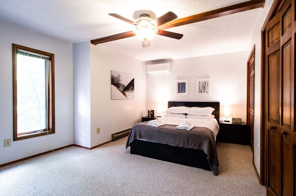 A bedroom with a bed, a ceiling fan, a window, and a door.