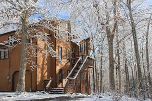 A wooden cabin with a staircase leading to the entrance, surrounded by snow-covered trees.