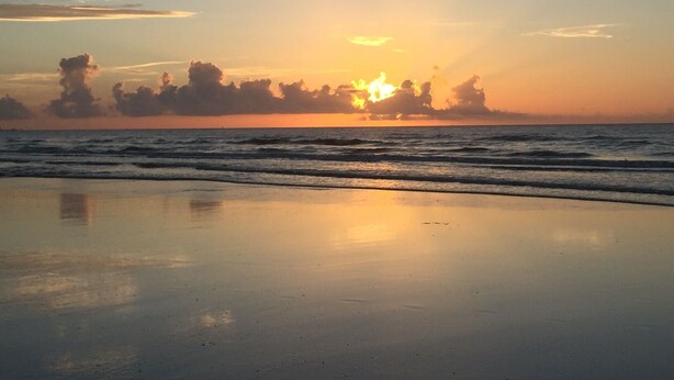 Una playa con olas tranquilas y una puesta de sol al fondo.
