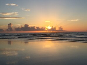 Una spiaggia con onde calme e un tramonto sullo sfondo.