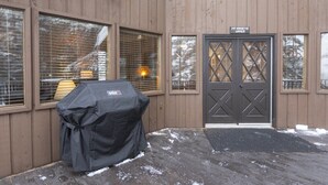 A wooden building with a covered grill, large windows, and a door labeled "McKinney's Upper." - Mountain View Duplex (Whitefish)