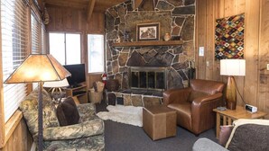 A cozy living room with a stone fireplace, leather furniture, and a television. - Mountain View Duplex (Whitefish)