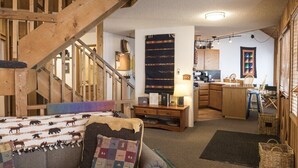 A cozy living room with a wooden staircase, a kitchen area, and a dining space. - Mountain View Duplex (Whitefish)