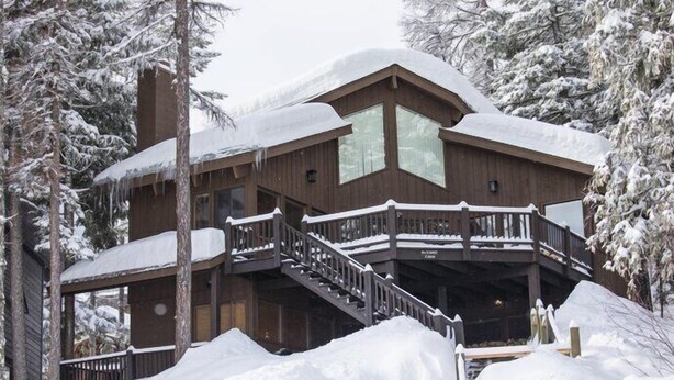 A wooden lodge with a balcony and a covered porch, surrounded by snow-covered trees. - Mountain View Duplex (Whitefish)