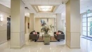 A spacious lobby with a high ceiling, a central seating area, and large windows allowing natural light.