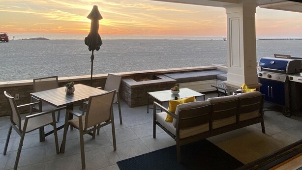A terrace with a view of the sunset over the water, outdoor seating, and a barbecue grill. - Luxury Oceanfront Home with Rooftop Deck, Hot Tub, Fire Pit (Newport Beach)