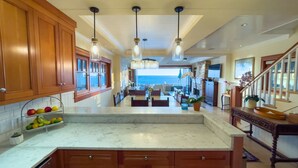 A spacious kitchen with wooden cabinets, a marble countertop, and pendant lighting. - Luxury Oceanfront Home with Rooftop Deck, Hot Tub, Fire Pit (Newport Beach)