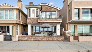 A modern two-story house with a stone facade, large windows, and a covered outdoor seating area. - Luxury Oceanfront Home with Rooftop Deck, Hot Tub, Fire Pit (Newport Beach)