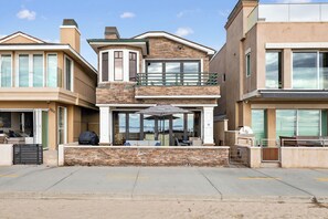 A modern two-story house with a stone facade, large windows, and a covered outdoor seating area. - Luxury Oceanfront Home with Rooftop Deck, Hot Tub, Fire Pit (Newport Beach)
