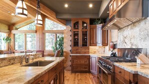 A spacious kitchen with wooden cabinets, granite countertops, and a large island with a sink. - Deer Valley Cabin W/ Hot Tub | Theater (Park City)