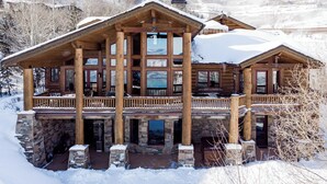 A large log cabin with a stone foundation, multiple balconies, and large windows. - Deer Valley Cabin W/ Hot Tub | Theater (Park City)