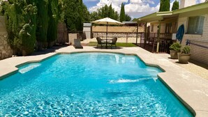 Una piscina rettangolare con acqua cristallina, circondata da un solarium in cemento e una recinzione in legno.