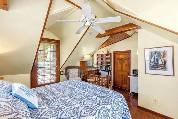Une chambre dotée d’un grand lit, d’un ventilateur de plafond, d’une kitchenette et d’un coin repas.