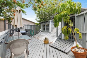 Une terrasse en bois avec une table et des chaises, un barbecue et une plante en pot.