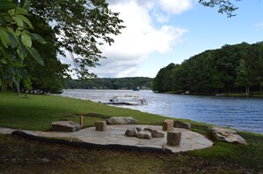 A riverside park with a stone patio, large rocks, and a grassy area. - Lake Front w/ 1.5 Acre Private Lot, Hot Tub, Paddle Boat, & Kayaks (DuBois)