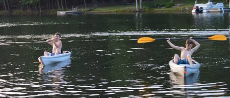 Two people in small boats on a calm lake with trees in the background.