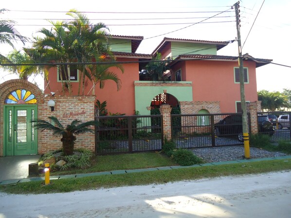 A two-story building with a green door, a brick entrance, and a small garden area with palm trees. - Apartment in Boracéia on the North Coast (Bertioga)