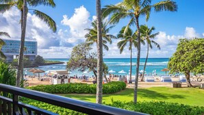 A beach view with palm trees, a pool area, and a building in the background. - SUMMER REDUCED! Villa 203 Ocean View Turtle Bay (Kahuku)