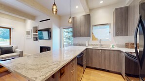 A modern kitchen with a marble countertop, wooden cabinets, and a built-in dishwasher. - Christophe Condo 503 - Year-round Outdoor Pool and Hot Tub and Bald Mt. Views (Ketchum)