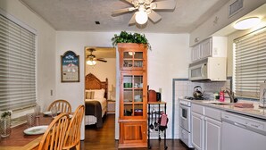 A compact kitchen with wooden cabinets, a dining area with a table and chairs, a built-in bookshelf, and a ceiling fan. - Sabal Palm Unit 1 1 Beach Getaway (Clearwater Beach)