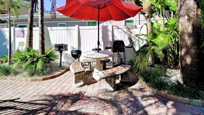 A patio with a red umbrella, a stone table, and a grill. - Sabal Palm Unit 1 1 Beach Getaway (Clearwater Beach)