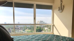 Une chambre avec une grande fenêtre, un lit recouvert d’une couvre-lit à motifs et une ancre fixée au mur.