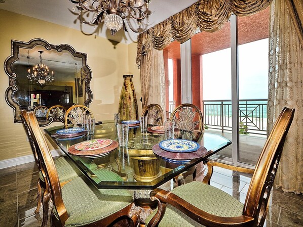 A dining area with a glass table, ornate chairs, and a large mirror.