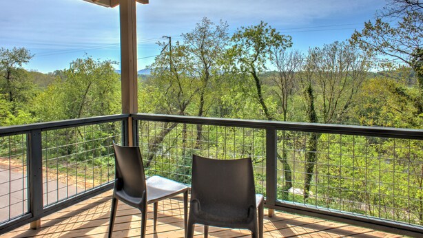 Een balkon met twee stoelen en een tafel, met uitzicht op een bebost gebied met heldere lucht.
