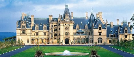 Um edifício grande e histórico com fachada simétrica, várias chaminés e uma entrada central.