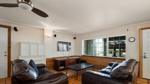 Ein Wohnzimmer mit Ledersofas, einem Couchtisch, einem Fernseher und einem Fenster mit Blick auf geparkte Autos.