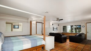Ein Schlafzimmer mit Himmelbett, einem kleinen weißen Schrank, einer schwarzen Ledersofa und einem großen Fenster mit Blick ins Freie.