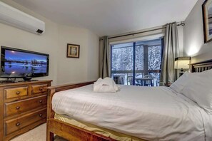 A hotel room with a bed, a television, a dresser, a window with a view of trees, and a framed picture on the wall. - Greystone Lodge 333 Ski-in/Out by Acer Vacations (Whistler)