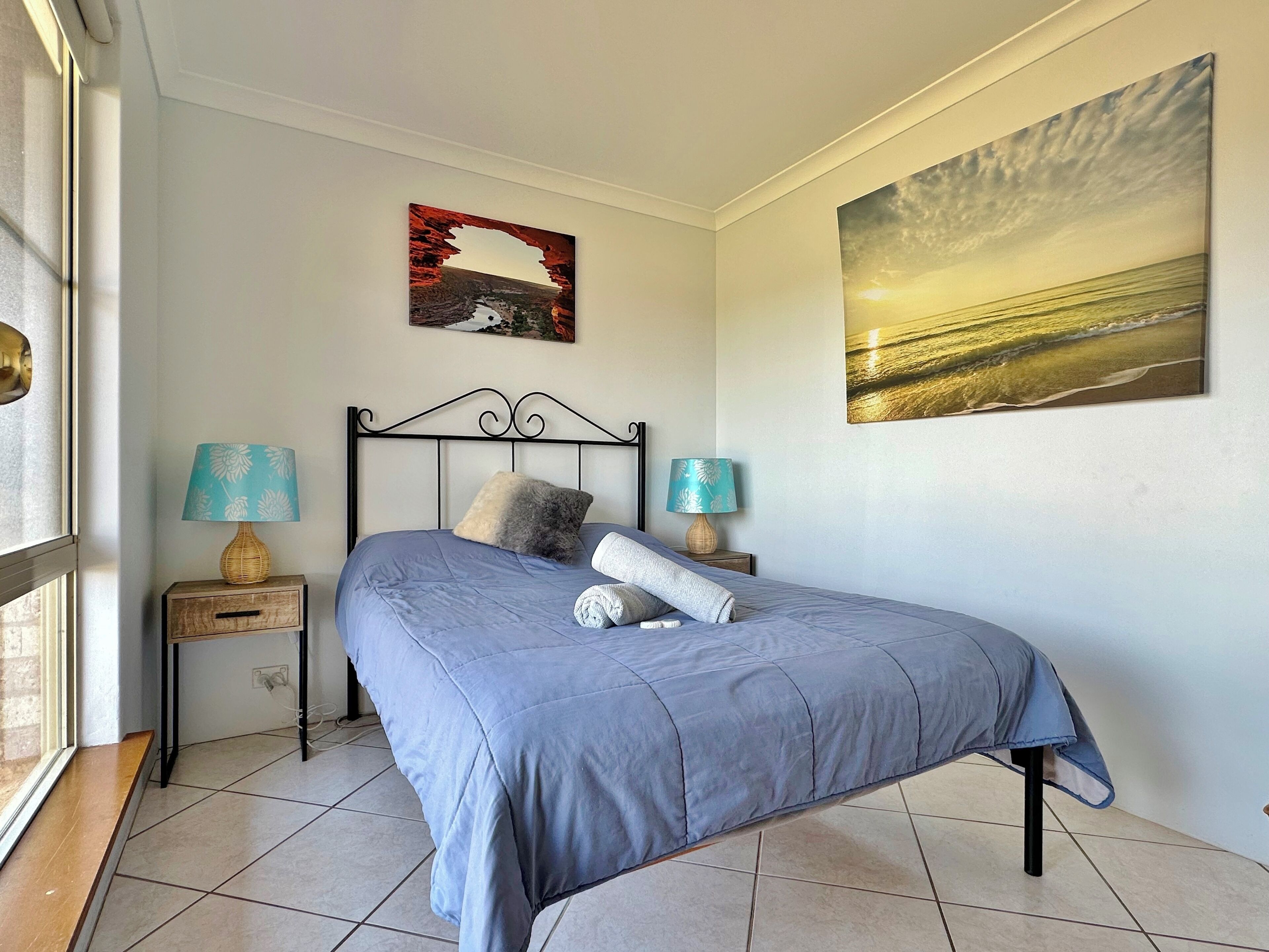 A bedroom with a bed, two bedside tables, a window, and two wall-mounted lamps.