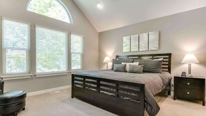 A bedroom with a large bed, two bedside tables, a bench, and a window with blinds.