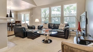 A modern living room with a sectional sofa, a glass coffee table, and a television.