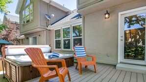 A deck with a hot tub, two Adirondack chairs, and a glass door leading to a covered patio.