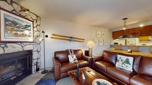 Een gezellige woonkamer met een open haard, leren banken, een salontafel en ski-uitrusting aan de muur.