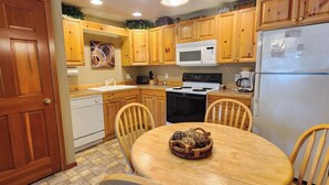 A kitchen with wooden cabinets, a microwave, a stove, a refrigerator, and a dining table with chairs.