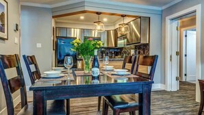 Un comedor con una mesa rectangular dispuesta para seis personas, rodeada de sillas, y un jarrón con flores sobre la mesa.